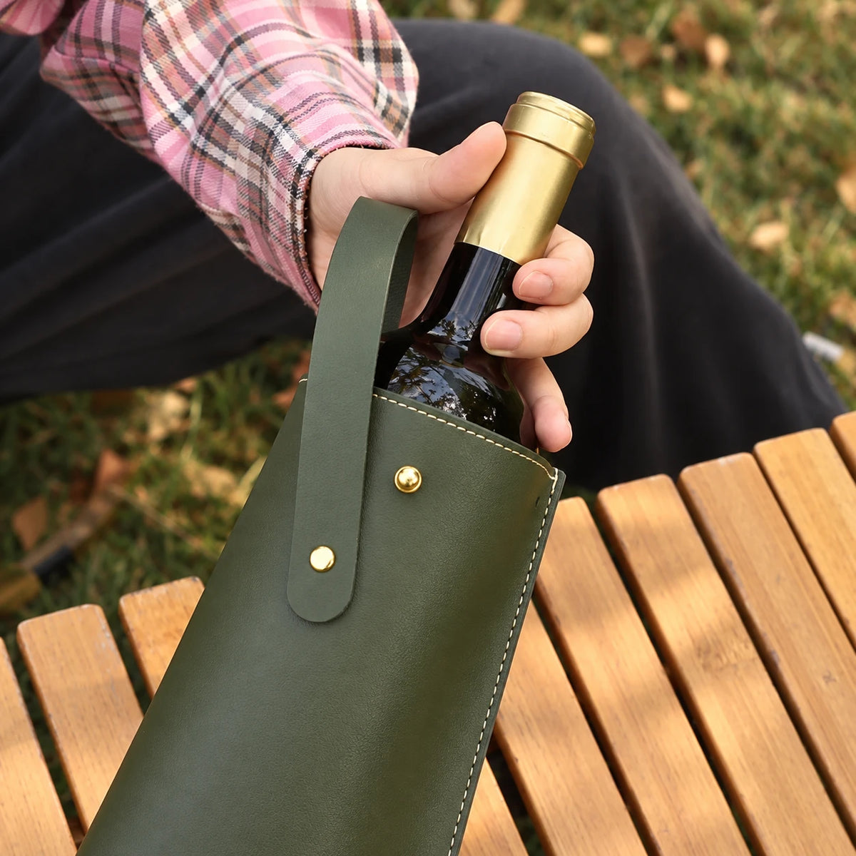 Sacando una botella de vino de la bolsa de ecocuero verde oliva en un picnic al aire libre
