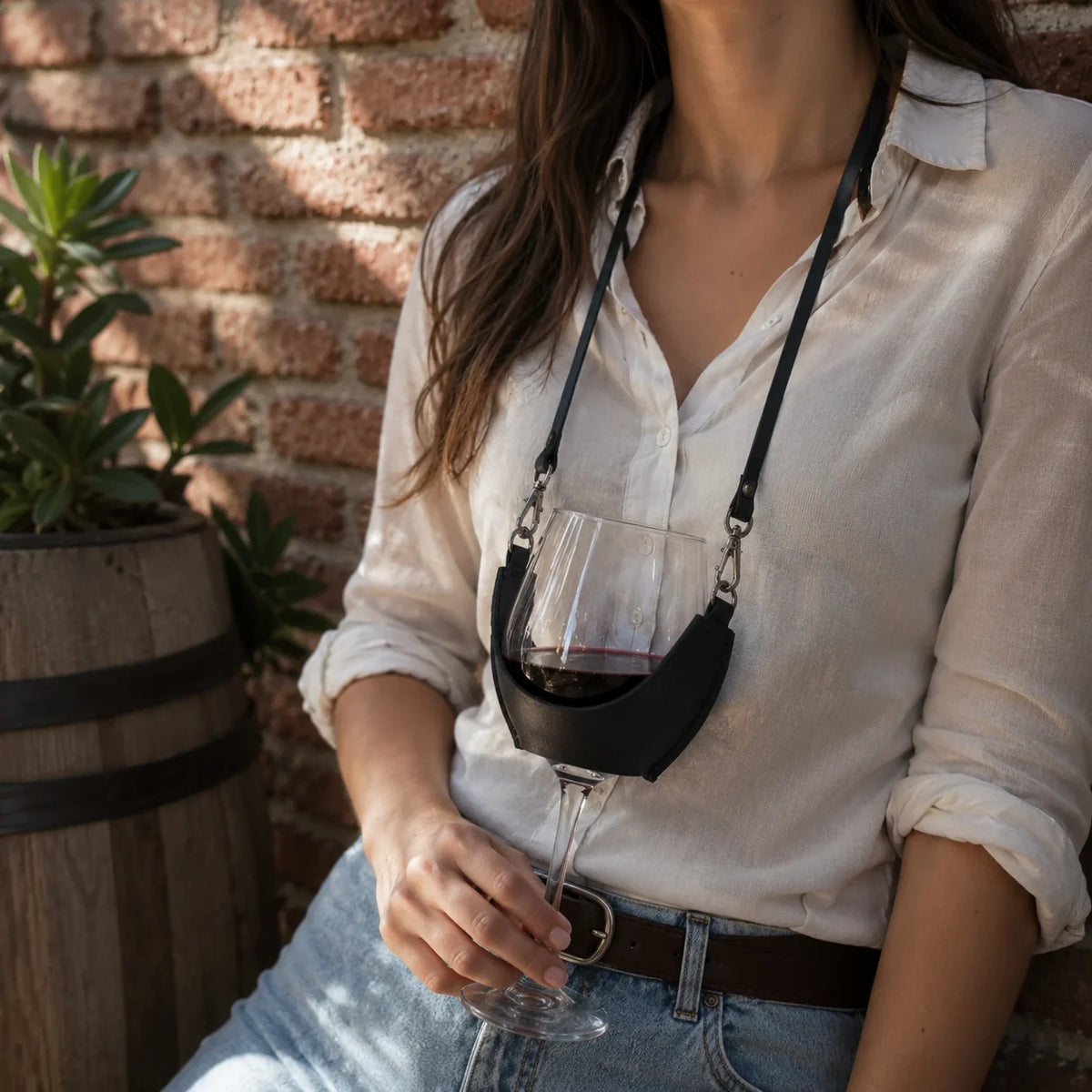 Mujer con el porta copas de cuero negro Wine Tree y una copa de vino tinto, junto a un muro de ladrillo