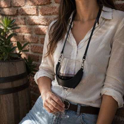 Mujer con el porta copas de cuero negro Wine Tree y una copa de vino tinto, junto a un muro de ladrillo